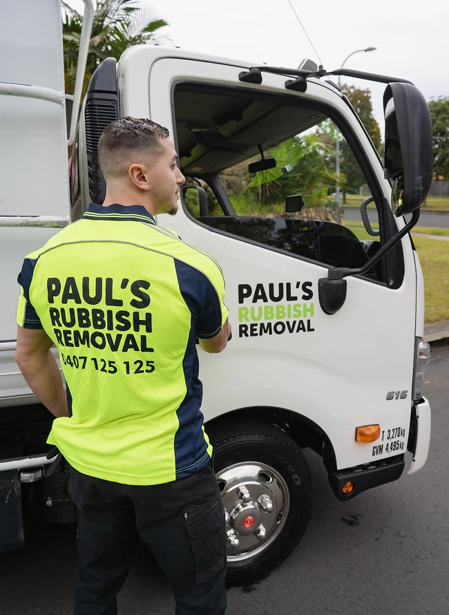 One of the crew opening the cab door of the loaded rubbish removal truck